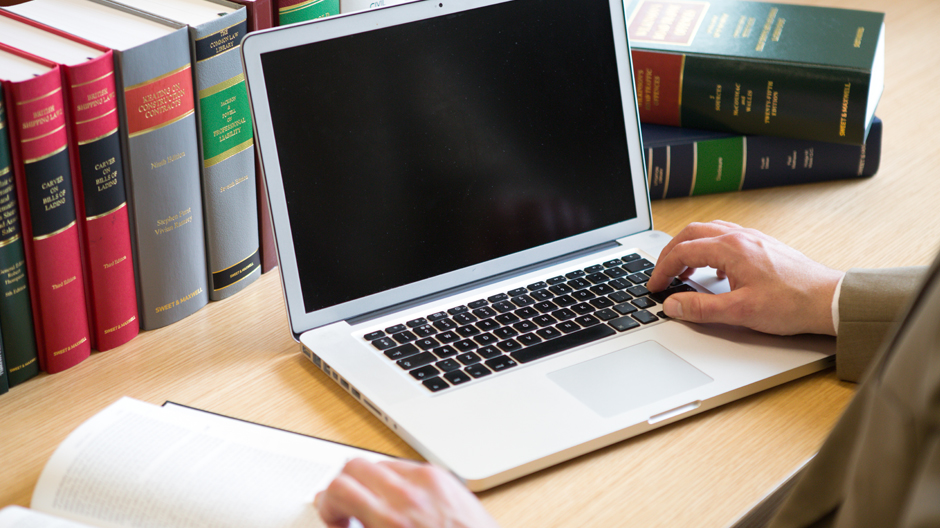 Man using laptop and referencing book in office
